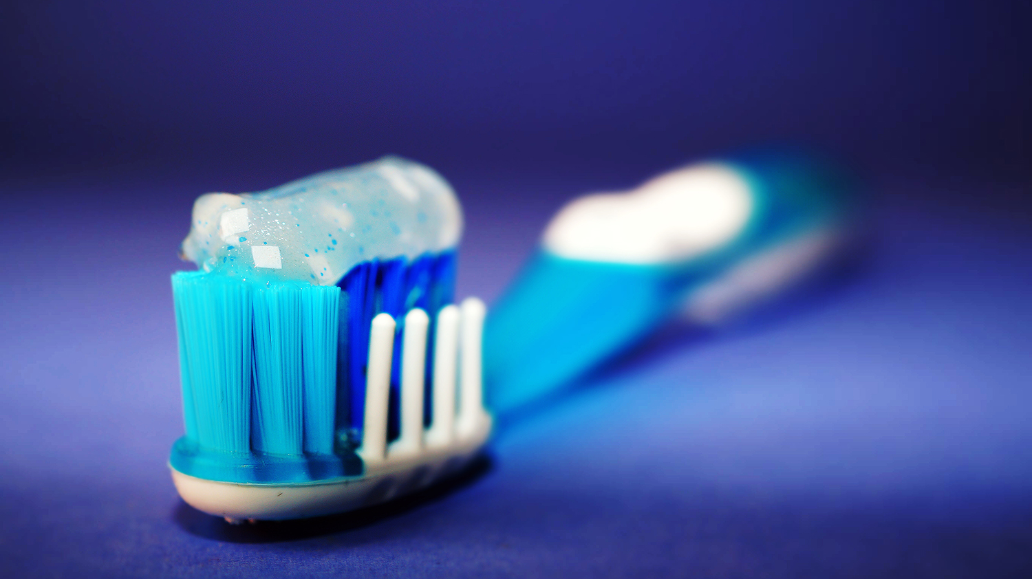 A toothbrush with toothpaste on it in front of a rich blue background